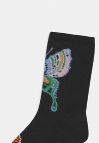 Meias pretas com um design colorido de borboleta, apresentando detalhes em azul, verde, laranja e preto. Textura de malha com ponta e calcanhar reforçados.