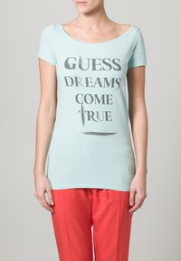 Hellblaues T-Shirt mit kurzen Ärmeln und rundem Ausschnitt. Zeigt den Text "GUESS DREAMS COME TRUE" in fetten grauen Buchstaben.