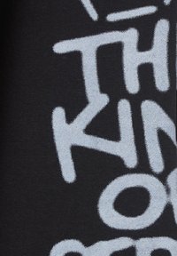 Czarna tkanina z dużym, wyraźnym, jasnoszarym tekstem przedstawiającym różne kształty i style. Miękka faktura, prawdopodobnie materiał mieszany bawełniany.