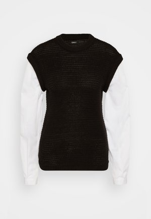 Pull en tricot noir à manches courtes et structurées superposé sur une chemise blanche. Présente un motif texturé et un col rond.