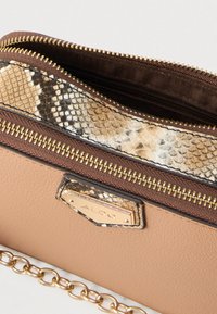 Pálená kožená kabelka barvy světle hnědé s pozlaceným řetízkem, horním zipem a texturovaným hadím potiskem v odstínech hnědé a krémové. Obsahuje pozlacené kovové logo.