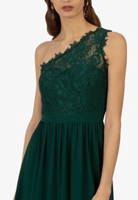 Grünes Spitzenkleid mit einseitigem Design, aufwendigen Blumenmustern und einem fließenden Rock mit gerafftem Bund.