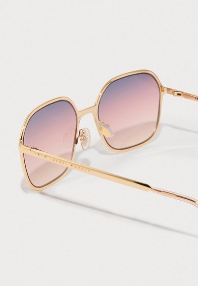 Gafas de sol de metal dorado con lentes de gradiente rosa, de forma cuadrada y con almohadillas para la nariz ajustables. La montura presenta un logotipo grabado en la patilla.