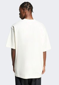 Cream-colored oversized t-shirt with short sleeves, made of soft cotton. Smooth texture and a rounded neckline. Back view shows a plain design.