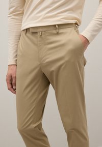 Pantalones beige ajustados de corte entallado, fabricados en tejido ligero. Cuentan con bolsillos laterales y pasadores para cinturón, con una textura suave.