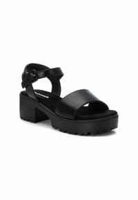 Sandalias de cuero negro con una tira frontal ancha, tira en el tobillo con hebilla y suela texturizada gruesa. La altura del tacón es moderada.