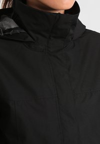 Black jacket with high collar, smooth texture, and visible seam details. Interior features a contrasting mesh lining. Minimalistic design.