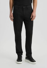 Schwarze Hose aus Baumwollmischung mit geradem Bein, Knopfverschluss und Seitentaschen, kombiniert mit schwarzen Sneakers.