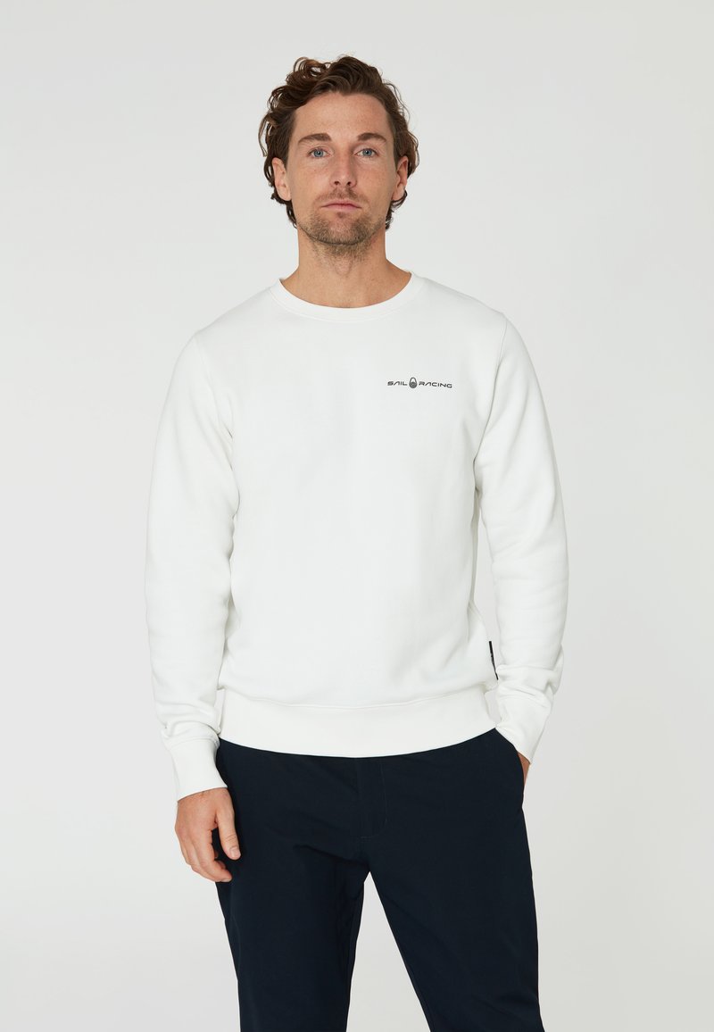 Sudadera blanca de manga larga con cuello y puños de canalé, que presenta un pequeño logo negro de "SAIL RACING" en el pecho. Textura suave.