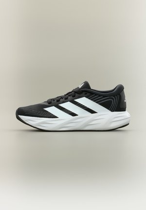 Chaussure de course noire avec motif à trois bandes blanches, semelle épaisse blanche et coussinée, et lacets noirs sur un fond neutre.