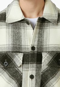 Rutig flanellskjorta i nyanser av vitt och grått, med svarta knappar, krage och två br östfickor. Mjuk textur med en mysig look.