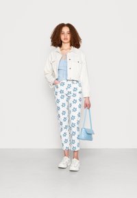 Jaqueta de ganga branca, blusa azul clara com laço, calças azul com padrão floral e mala azul clara. Ténis claros completam o visual.