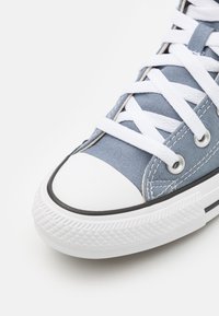 Ljusräktig kanvas sneaker med vita snören, gummitåhätta och texturerad vit sula med svarta accenter.