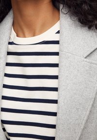 Gray wool-blend coat drapes over a white and navy striped T-shirt. The coat features a structured lapel and textured fabric.