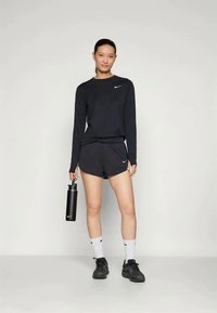 Zwart long-sleeve shirt en shortset met Nike-logo; houdt een zwarte waterfles vast; draagt zwarte schoenen en witte sokken.