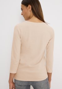 Haut couleur beige clair à manches longues avec un col rond et une coupe ample. Tissu en coton lisse sans motifs visibles. Design simple et ourlet droit.