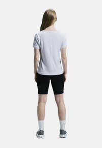 Vit atletisk t-shirt med avslappnad passform och korta ärmar, tillsammans med svarta åtsittande shorts och grå sneakers. Vita strumpor synliga.