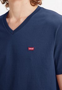 Mørkeblå V-hals T-shirt lavet af bomuld, med et lille rødt broderet Levis-logo på venstre brystområde. Korte ærmer.