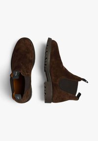 Botas Chelsea de ante marrón con paneles laterales elásticos, punta redonda, lengüeta y suela de goma texturizada. Diseño clásico con un color rico.