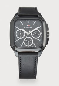 Montre-bracelet carrée noire avec un bracelet en cuir noir, aiguilles blanches, trois sous-cadrans et logo Hilfiger en dessous de l'indicateur de 12 heures.