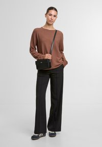 Hnědý, ribbovaný svetr s širokým výstřihem, kombinovaný s černými, dobře střiženými kalhotami. Drží malou černou crossbody tašku. Tenisky se pruhy.