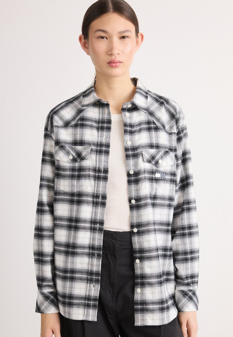 Camisa de franela a cuadros en blanco y negro con cierre de botones, dos bolsillos en el pecho y un diseño de yugo de estilo occidental. Textura suave y corte relajado.