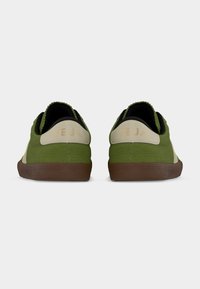 Ζευγάρι πράσινα και μπεζ αθλητικά παπούτσια Veja με καφέ σόλες, εμφανιζόμενα από πίσω σε απλό λευκό φόντο.