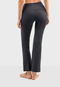 Pantalons de yoga noirs avec une taille haute, fabriqués en tissu lisse et extensible. Présentent une coupe ajustée avec une légère évasement au niveau de la cheville.