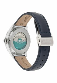 Reloj de acero inoxidable con fondo transparente, correa de piel azul oscuro y hebilla plateada. Presenta una esfera en color teal con grabado detallado.