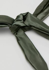 Olivgrüner Satinstoff, der zu einem Knoten gebunden ist, zeigt eine glatte Textur und einen dezenten Glanz. Das Design verfügt über zwei verlängerte, spitz zulaufende Enden.