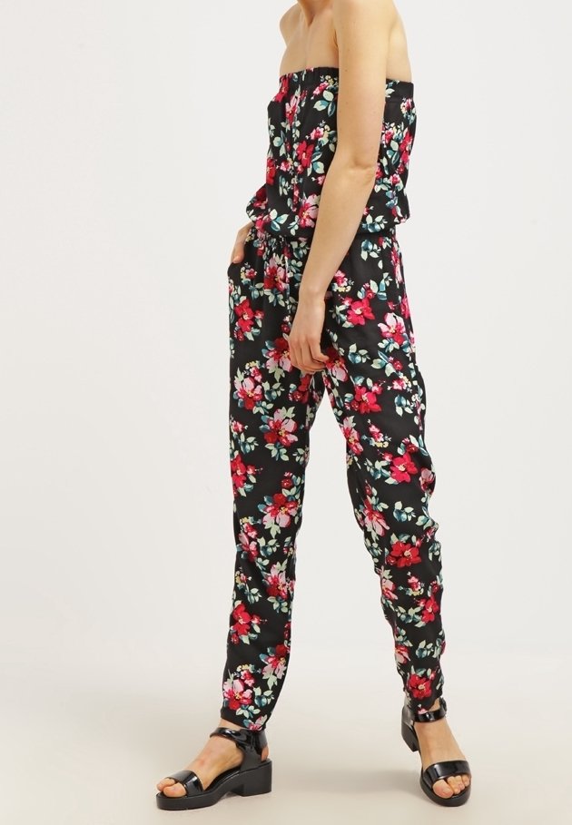 Blommig jumpsuit med off-shoulder design, svart bakgrund, livfulla rosa och blå blommönster och en avslappnad passform med bälte.