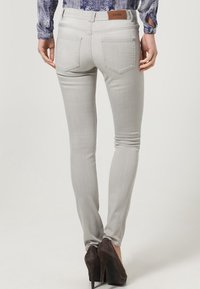 Ljusgrå skinny jeans med en slät textur och femficksdesign, med en brun läderlogotyp på midjan.
