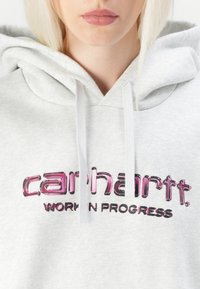 Grey hoodie with a drawstring, featuring a glossy pink and black "carhartt" logo and "WORK IN PROGRESS" text printed on the front.