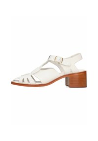 Sandalia de piel blanca con punta abierta, diseño recortado, correa ajustable en el tobillo y un bajo tacón de madera.