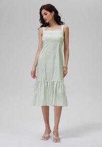 Robe à pois vert clair avec ourlet en dentelle, corsage ajusté, larges bretelles et ourlet à volants en tiers. Fabriquée en tissu lisse et léger.