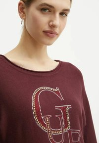 Felpa color marrone con scollo ampio e lettere decorate con strass dorati e argentati. Tessuto morbido, vestibilità comoda.