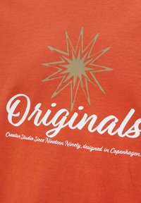 Orange bomuld t-shirt med et stort guldstjerne grafik og hvid tekst, der skriver "Originals" og "Creative Studio Since Nineteen Ninety."