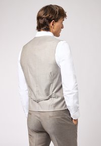 Helles graues, maßgeschneidertes Weste aus strukturiertem Stoff mit einem gerafften Rückendetail, getragen über einem weißen Hemd, das eine moderne Passform zeigt.