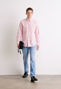 Gaiši rozā krekliņš ar garām piedurknēm, gaiši zili džinsi, melnas kurpes un neliela melna soma. Gluda auduma, ar pogu aizdari, ikdienas piegriezums.