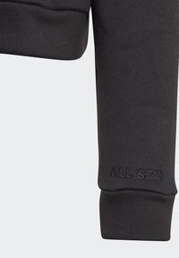 Il maniche del sudario nero presenta un tessuto testurizzato con polsino a coste; include il testo in rilievo "ALL SZN" sul bordo inferiore.