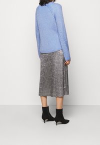 Světlomodrý pletený svetr s dlouhými rukávy, doplněný stříbrnou plisovanou midi sukní a černými kotníkovými botami. Viditelná texturovaná látka a detaily.