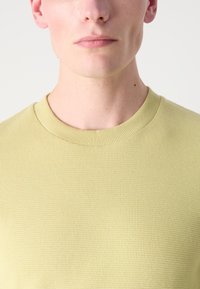 Lys gul teksturert genser med ribbestrikket rund hals, tettsittende design og jevn overflate. Har en tettsittende stil.