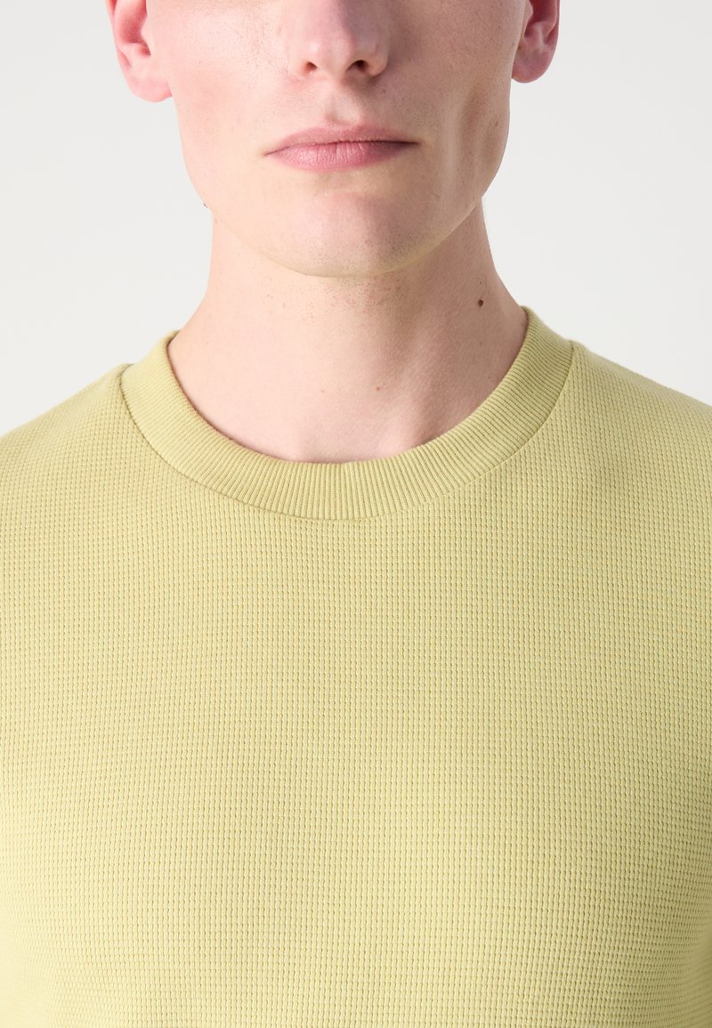 Lys gul sweatshirt med struktur, ribbet rund halsudskæring, tætsiddende design og glat overflade. Har en tætsiddende stil.