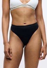 Sorte tanga underbukser med en glat tekstur, prydet med et Calvin Klein-logo på livet. Slank, minimalistisk design og højt skårne benåbninger.