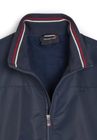 Granatowa kurtka zapinana na zamek z prążkowanym kołnierzem, ozdobiona czerwonymi i białymi paskami. Wnętrze z mikrowentylowanej tkaniny. Widoczna metka marki wewnątrz.