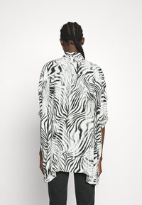 Svartvitt zebra-mönstrat oversized skjorta med hög-låg nederkant, korta ärmar och krage, tillverkad av ett lätt tyg.
