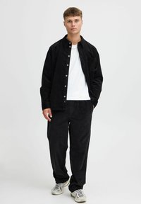 Black corduroy shirt with buttons, paired with matching pants. White t-shirt underneath, featuring casual sneakers with a textured design.