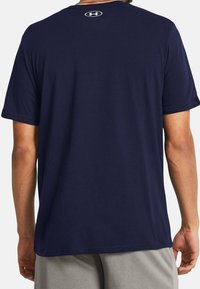 Námořnické modré tričko vyrobené z měkké tkaniny, s krátkými rukávy a kulatým výstřihem. Na zádech je bílé logo Under Armour na krku.