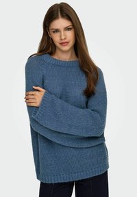 Niebieski sweter dziergany z szerokim okrągłym dekoltem i luźnymi rękawami. Materiał wydaje się miękki i teksturowany, z prążkowanym wykończeniem u dołu.