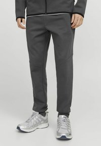 Gray athletic pants with a fitted design, featuring contrasting stitching, side pockets, and smooth texture. Paired with silver sneakers.
